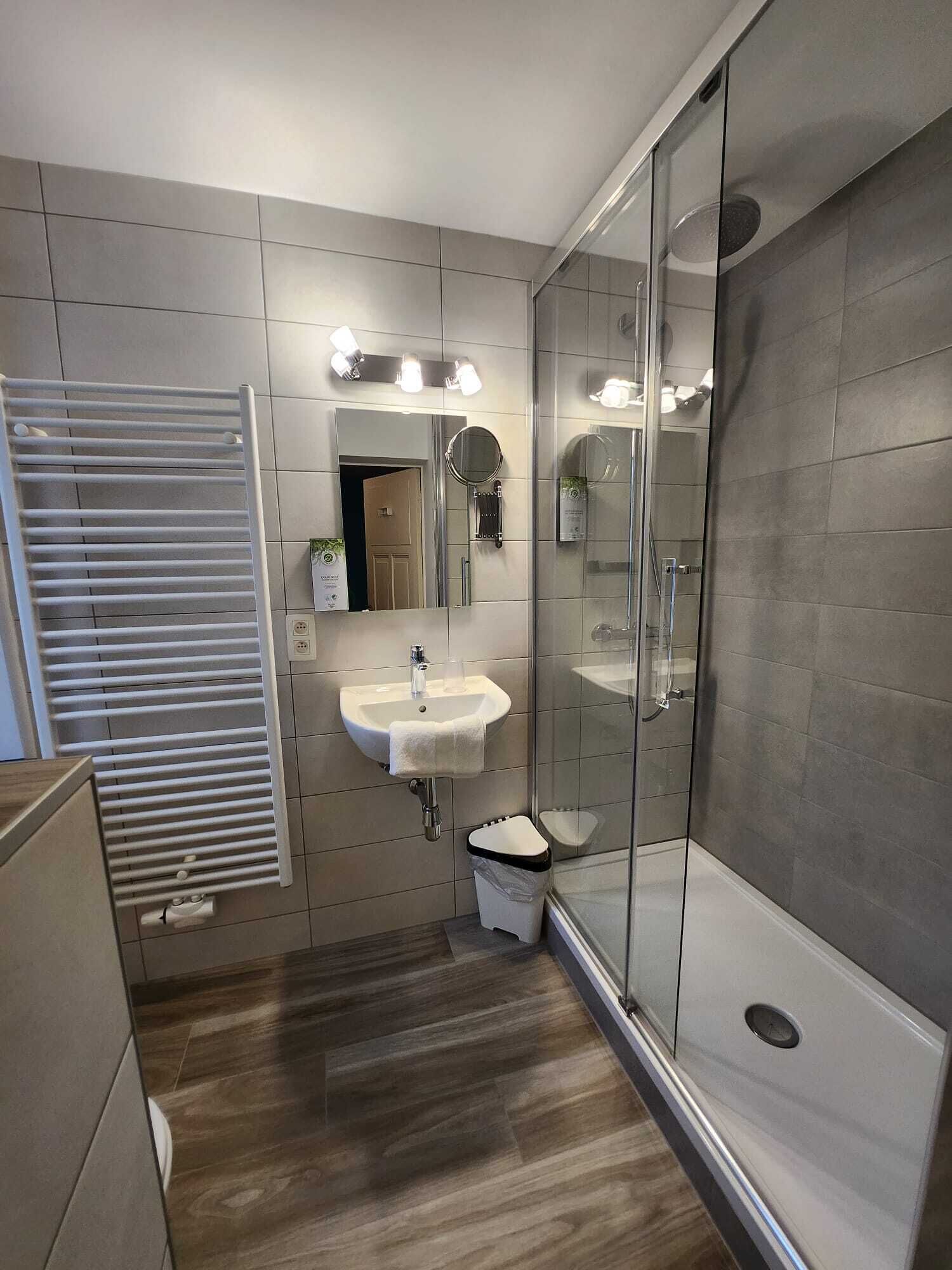 A modern bathroom with a glass shower enclosure, a white sink with a mirror, and a towel rack.
