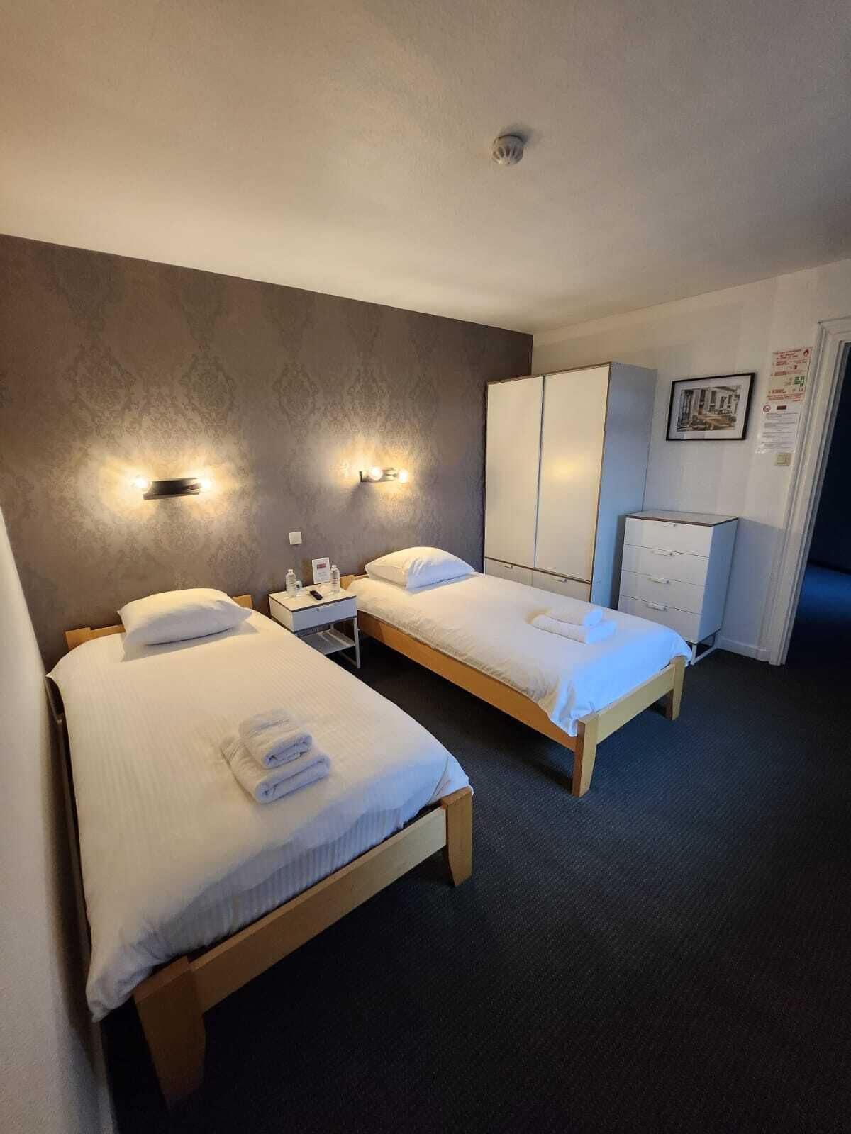 Habitació d'hotel amb dos llits individuals, un armari, escriptori amb cadira i una tauleta de nit.