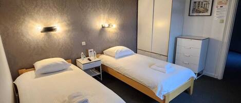 Habitació d'hotel amb dos llits individuals, un armari, escriptori amb cadira i una tauleta de nit.
