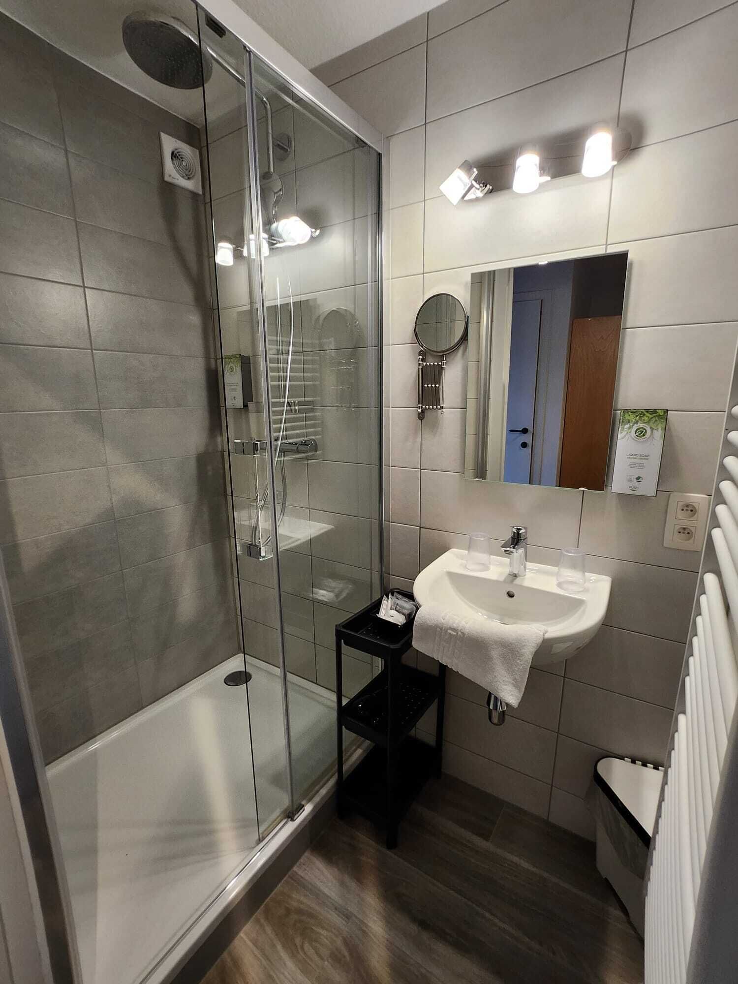 A modern bathroom with a glass shower enclosure, a white sink, and a small vanity.