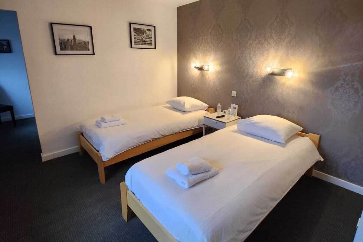 A hotel room with two single beds, a nightstand with a lamp, and two framed pictures on the wall.