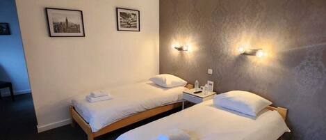 A hotel room with two single beds, a nightstand with a lamp, and two framed pictures on the wall.