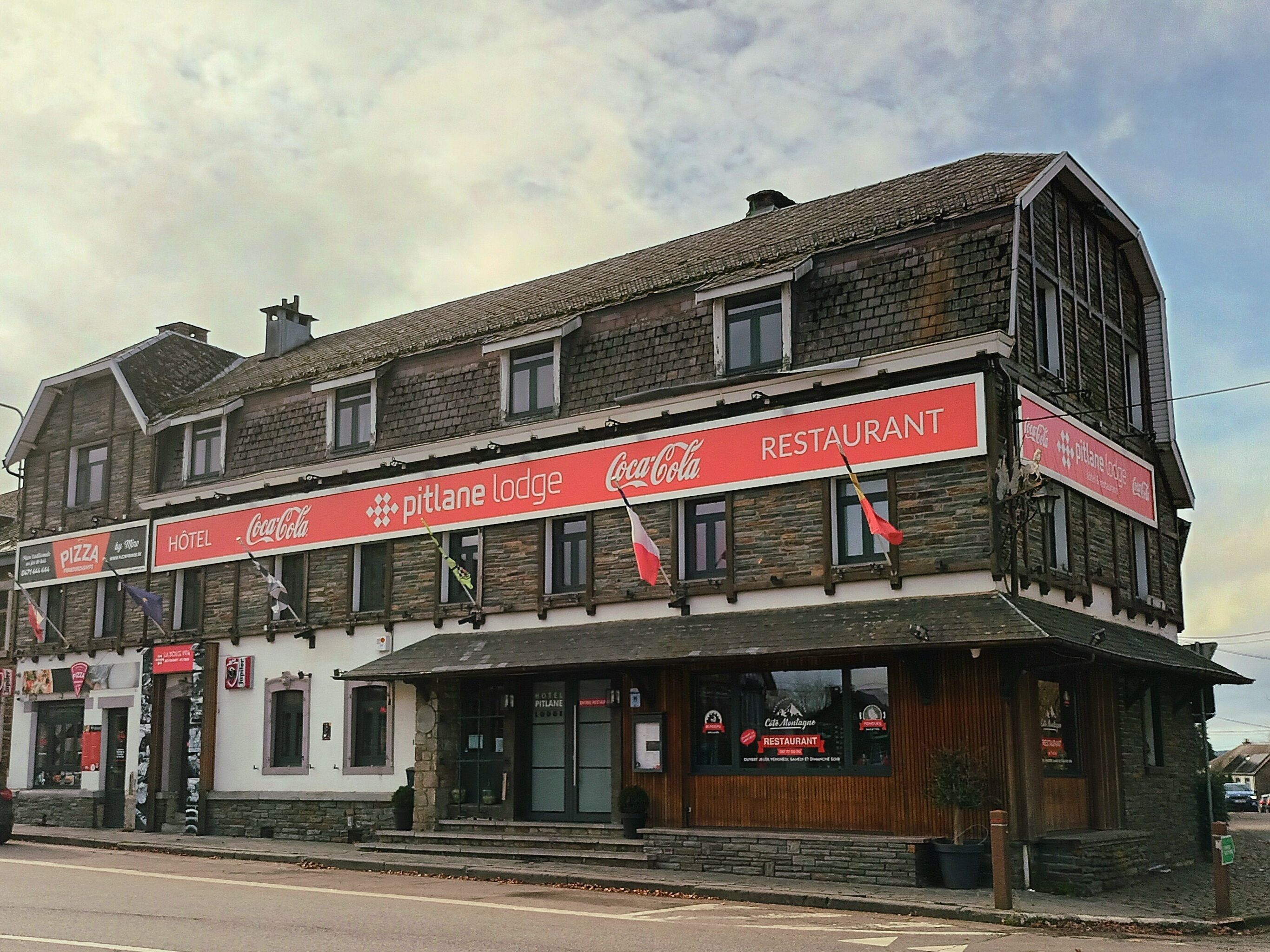 A two-story building with a Coca-Cola sign and a 'Pitlane Lodge' sign.