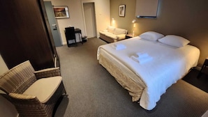 A hotel room with a large bed, a chair, a desk, and a door. - Pitlane Lodge (Stavelot)