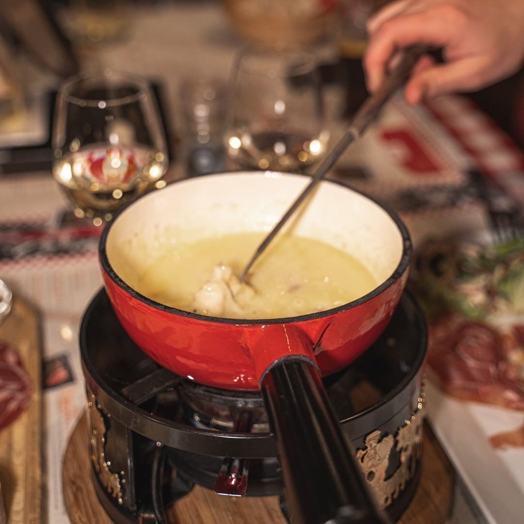 Une casserole rouge posée sur un réchaud portable, avec une cuillère à l’intérieur, le tout placé sur une surface en bois.