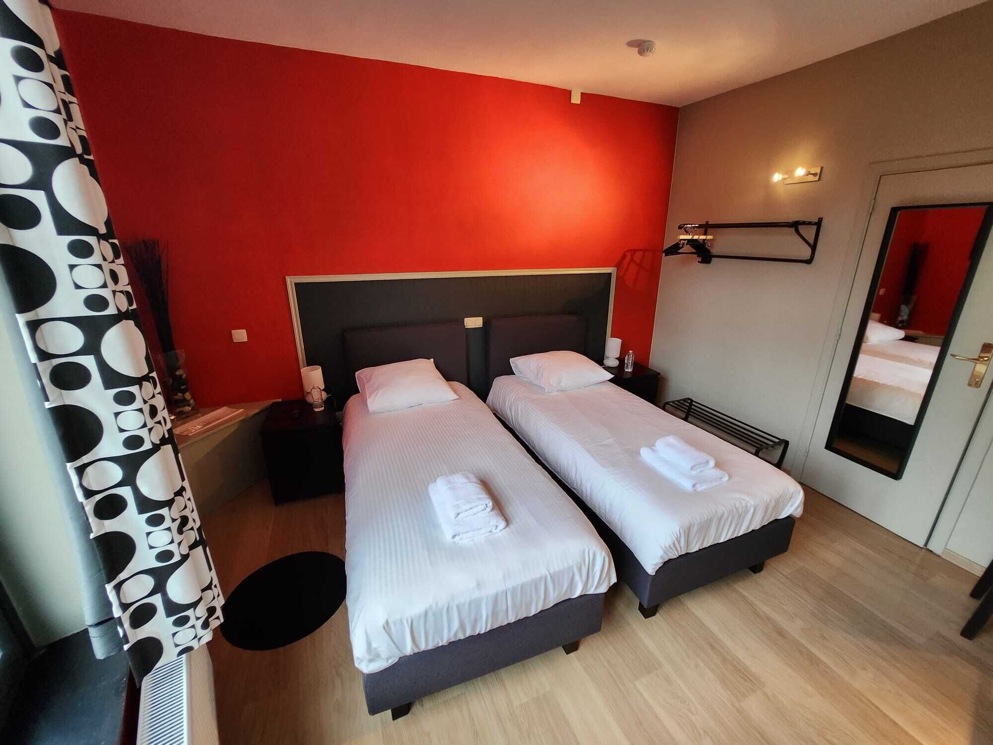A hotel room with two beds, a red wall, a mirror, and a black and white patterned curtain.
