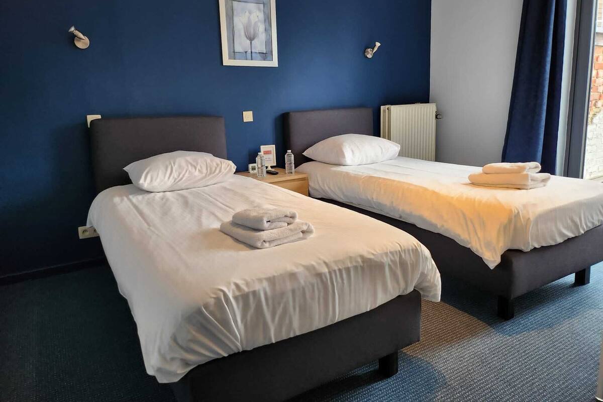 A hotel room with two beds, white linens, a framed picture on the wall, and a window with curtains.