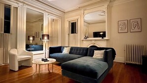 Una sala de estar con un sofá seccional azul oscuro, un sillón blanco, una mesita de centro redonda y una chimenea.