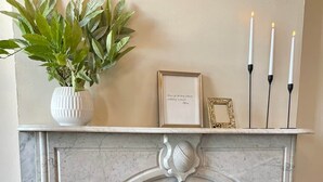 Una chimenea con repisa blanca, una cita enmarcada y tres velas encendidas.