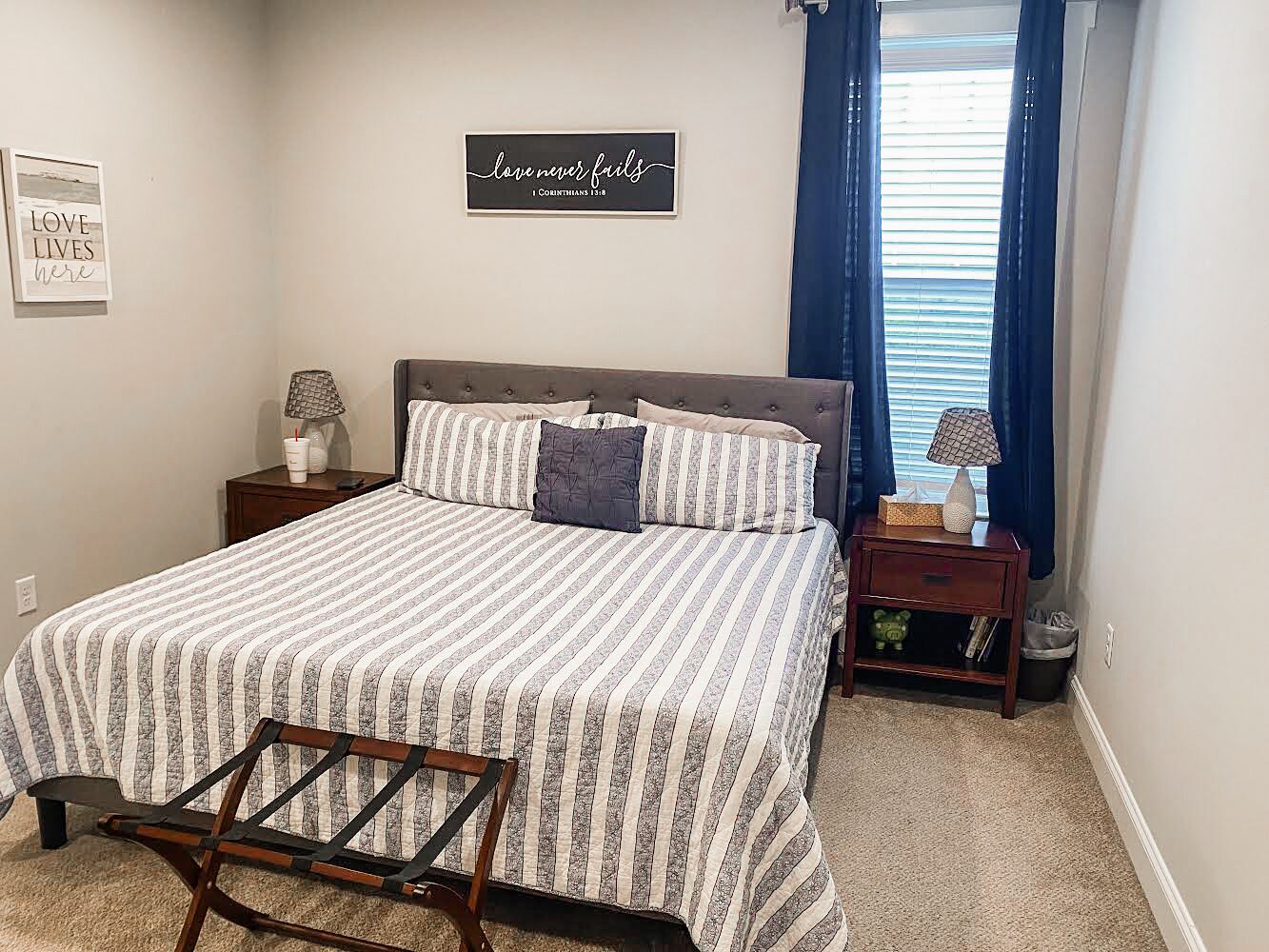 A bedroom with a bed, a nightstand, a lamp, a chair, and a wall with a quote.