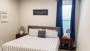 Un dormitorio con cama, mesita de noche, lámpara, silla y una pared con una cita.