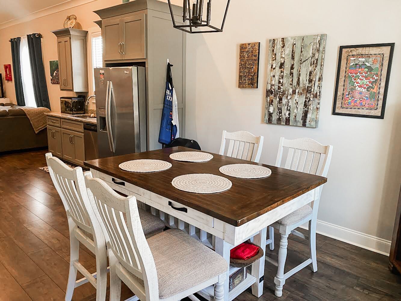 Un coin repas avec une table en bois, des chaises blanches et une cuisine en arrière-plan.