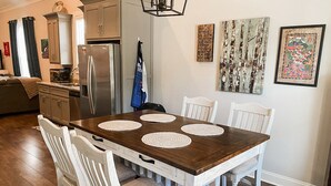 Un comedor con una mesa de madera, sillas blancas y una cocina al fondo.
