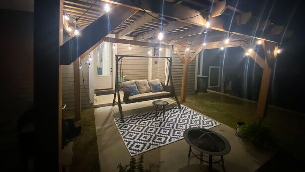 Un patio techado al aire libre con una silla mecedora, una mesa redonda y un tapete estampado.
