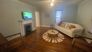 A living room with a fireplace, a television, a white sofa, and a round coffee table. - Vintage Cottage less than 3 mi from Duke Hospital (Durham)