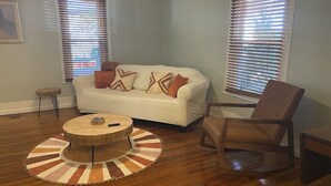 A living room with a white sofa, a brown armchair, a wooden coffee table, and a patterned rug. - Vintage Cottage less than 3 mi from Duke Hospital (Durham)