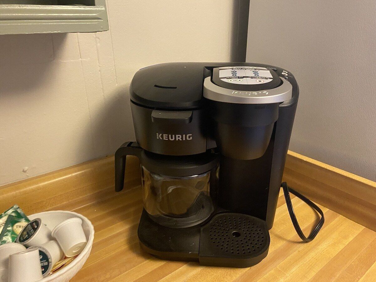 Keurig-kahvinkeitin puupintaisella työtasolla, jossa on kahvikapselihylly ja kuppi.