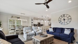 Ein modernes Wohnzimmer mit einem blauen Sofa, gestreiften Sesseln, einem Holztisch und einer großen Wanduhr.