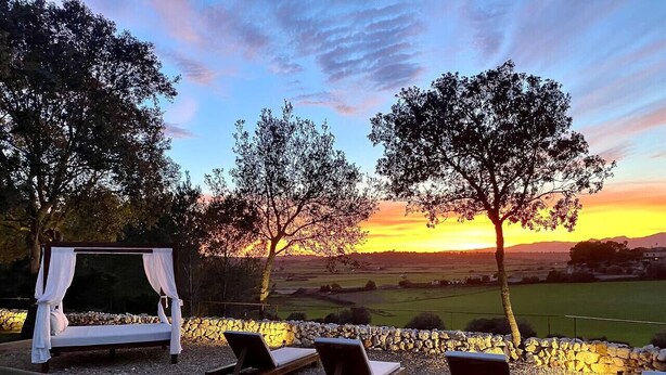 Un jardín con cama y sillones de descanso, una cama con dosel y vistas al atardecer sobre un paisaje.