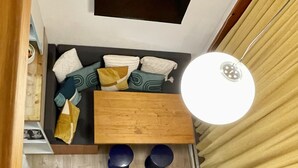 A compact living space with a sofa, a small table, a pair of shoes, and a hanging light fixture. - Apartment Mezzanine Perriand Arcs 1800 Valley View (Les Arcs 1800)