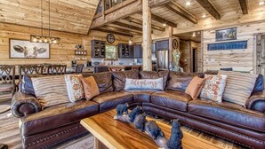 A cozy log cabin interior with a large leather sectional sofa, wooden beams, and rustic decor. - Huge Mountain LOG Cabin with Amazing Views (Gatlinburg)