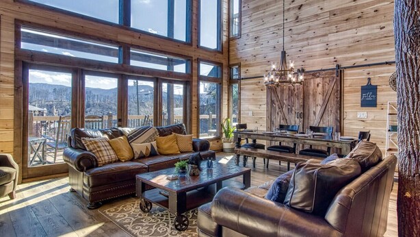 Un salon spacieux doté d’une grande fenêtre, d’un plafond en bois et d’un coin salon confortable avec un canapé et des fauteuils.