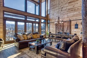 Un salon spacieux doté d’une grande fenêtre, d’un plafond en bois et d’un coin salon confortable avec un canapé et des fauteuils.