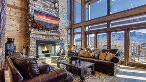 Un salon spacieux doté d’une cheminée, de canapés en cuir et de grandes fenêtres offrant une vue sur les montagnes.