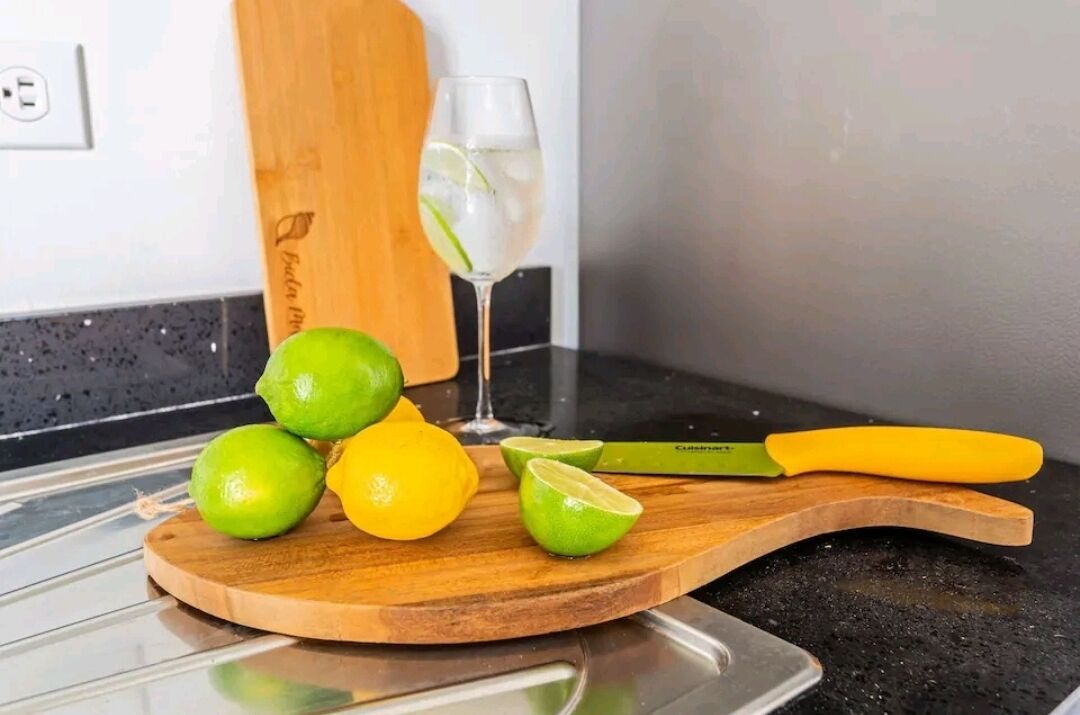 A wooden cutting board with limes and a glass of water on a kitchen counter.