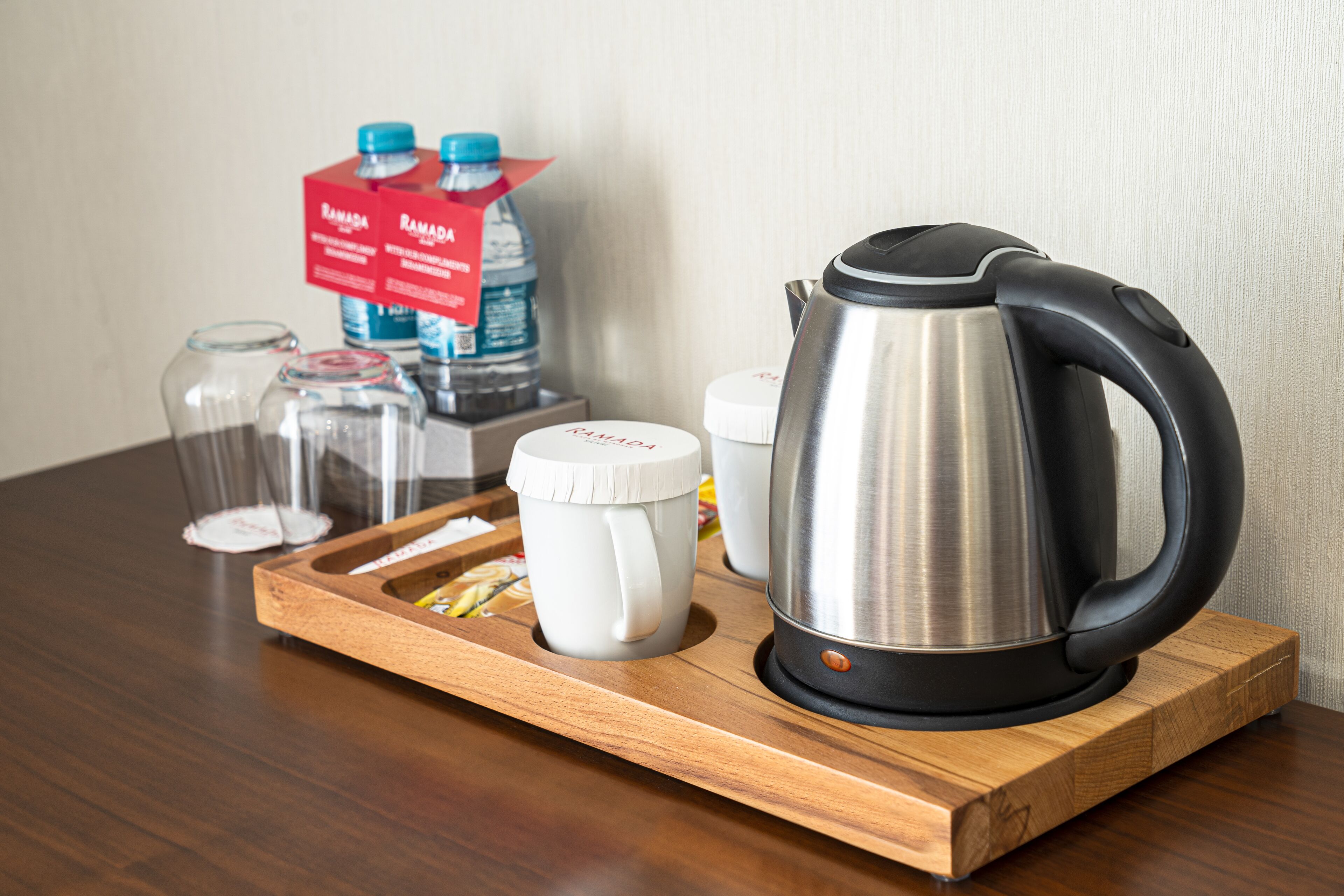 Un plateau en bois sur lequel se trouvent une bouilloire, une tasse, un bocal en verre et une bouteille d’eau.