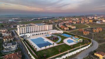 Vista aérea de un hotel con varias edificaciones, una piscina y un área ajardinada con palmeras.
