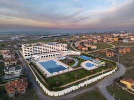 Vista aérea de un hotel con varias edificaciones, una piscina y un área ajardinada con palmeras.