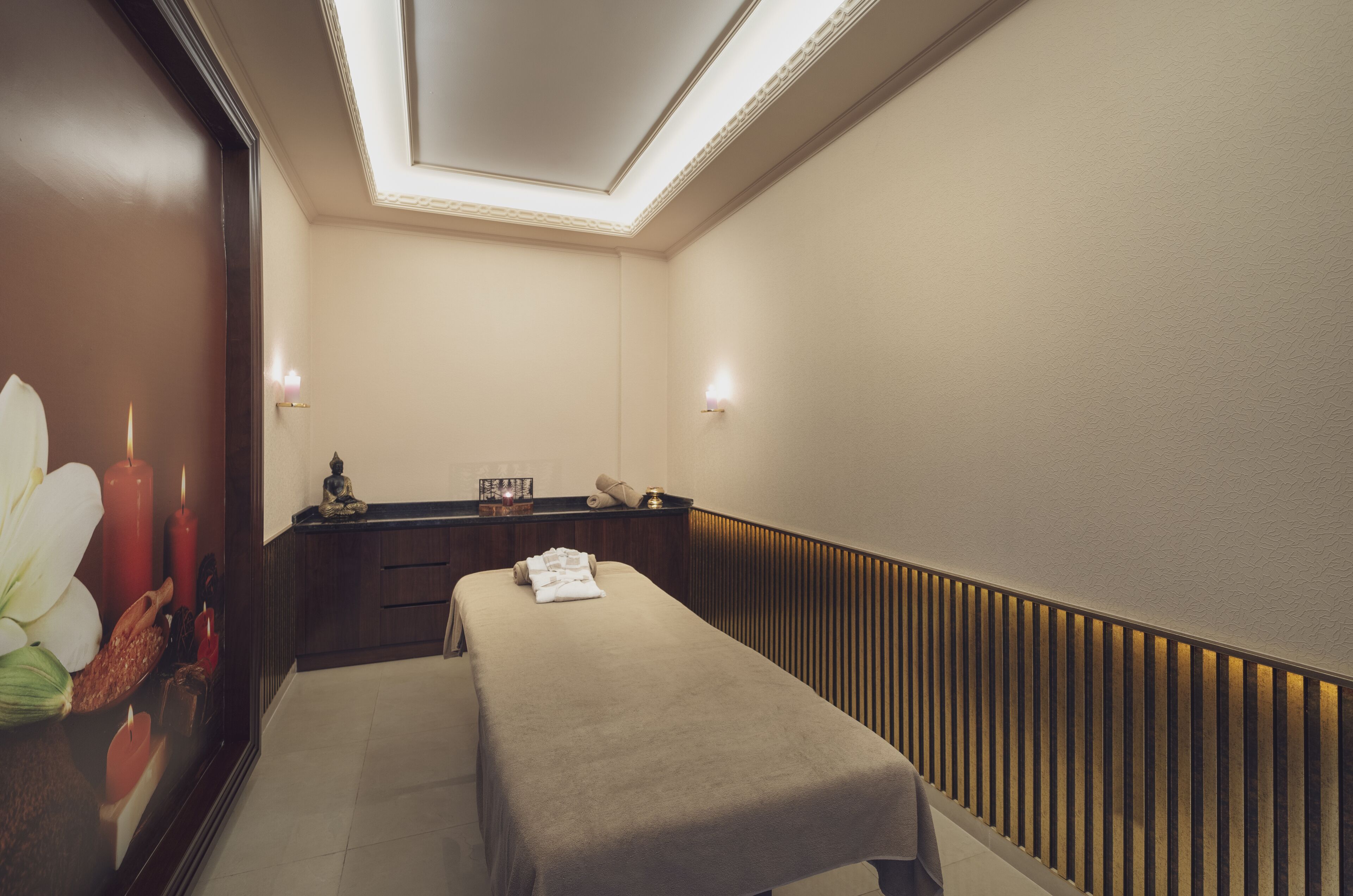 Un cuarto de spa con una camilla de masaje, velas y un adorno en la pared.