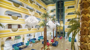 A spacious lobby with multiple seating areas, palm trees, and a grand chandelier.