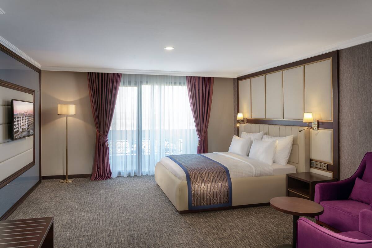 Een hotelkamer met een groot bed, een bureau, een stoel, een televisie en uitzicht op de stad.