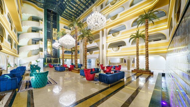 A spacious lobby with multiple seating areas, palm trees, and chandeliers.