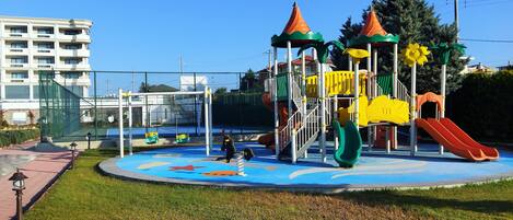 Un parque infantil con toboganes y estructuras para escalar, rodeado por una valla y césped.