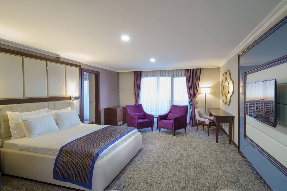 Een hotelkamer met een groot bed, twee fauteuils, een bureau en een televisie aan de muur.