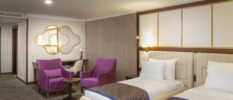A hotel room with two beds, a purple armchair, a small round table, and a wall-mounted lamp.