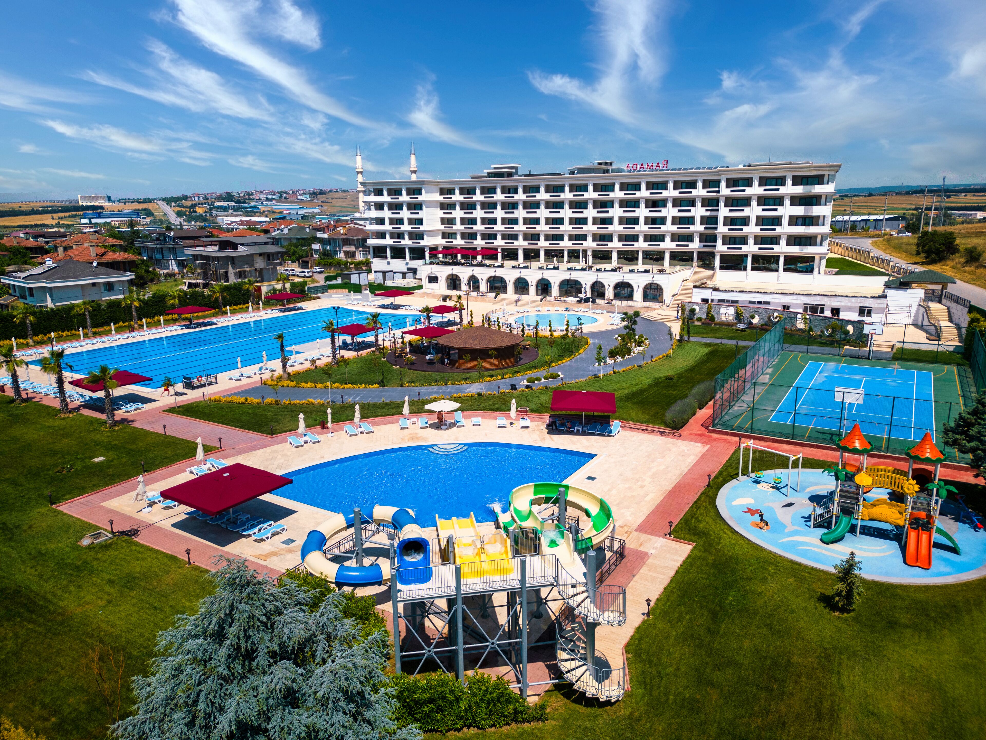 Um hotel com uma piscina grande, área de recreação infantil e quadra de tênis.