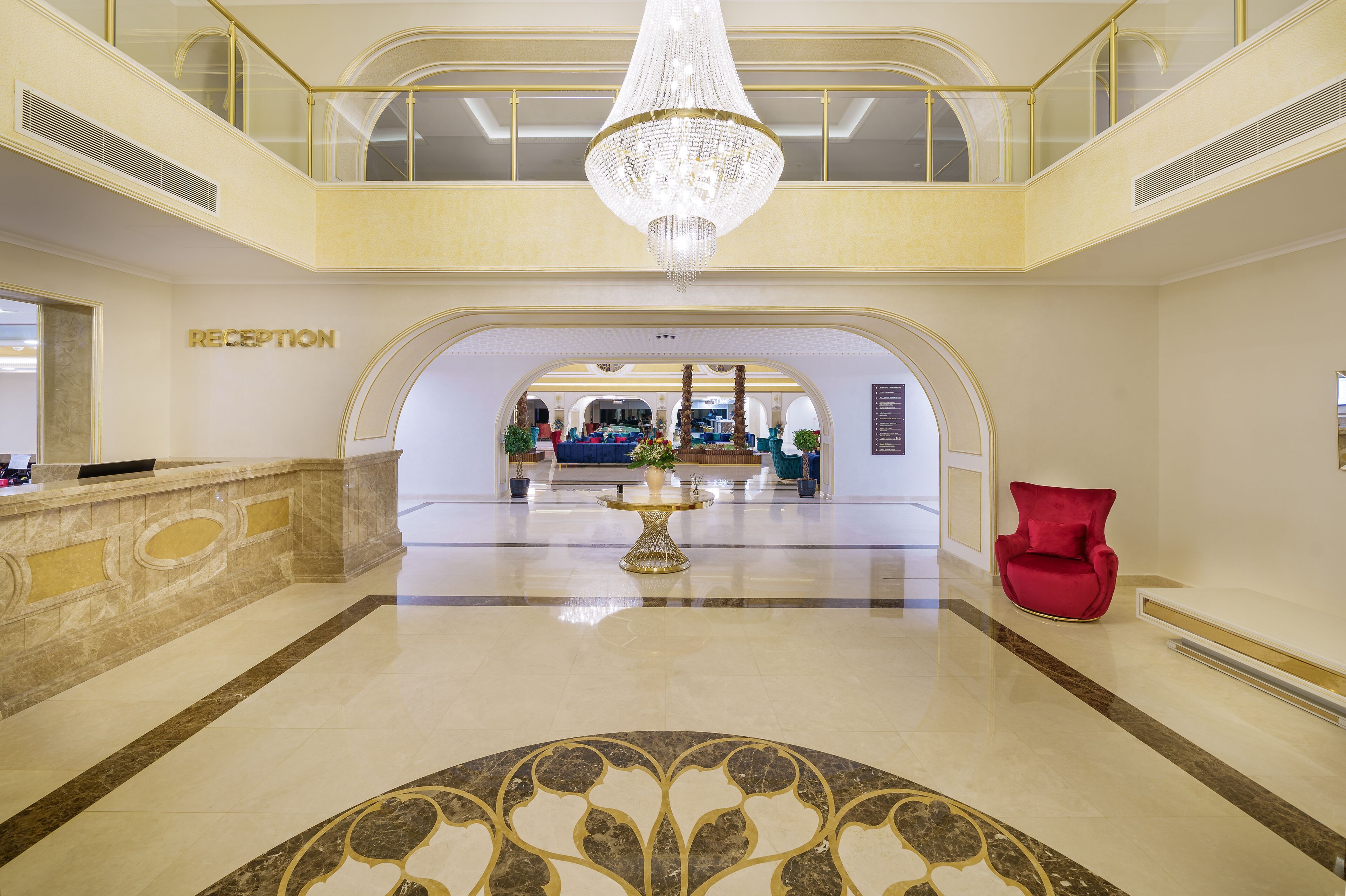 En rummelig lobby med reception, lysekrone og en rød stol.