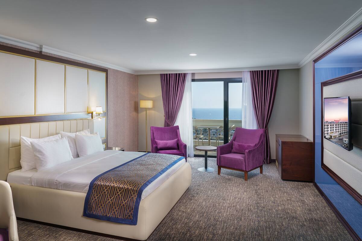 Een hotelkamer met een groot bed, twee paarse fauteuils, een kleine tafel en een televisie aan de muur.