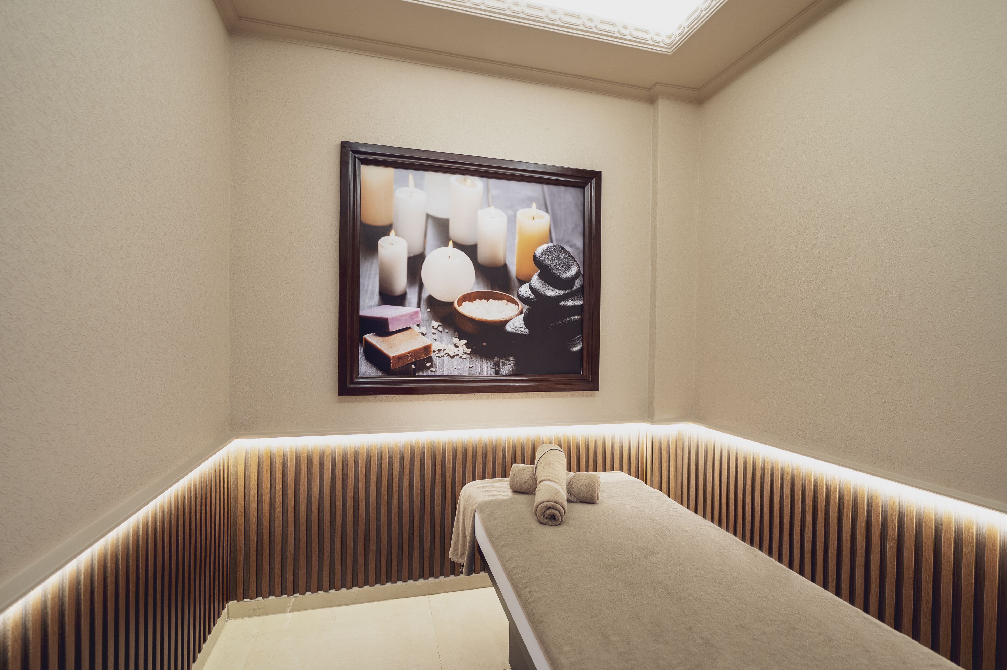 Une salle de spa équipée d’une table de massage, d’une œuvre d’art encadrée représentant des bougies et d’un banc en bois.