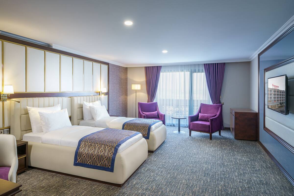 Een hotelkamer met twee bedden, een zithoek met een tafel en stoelen, en een aan de muur bevestigde televisie.