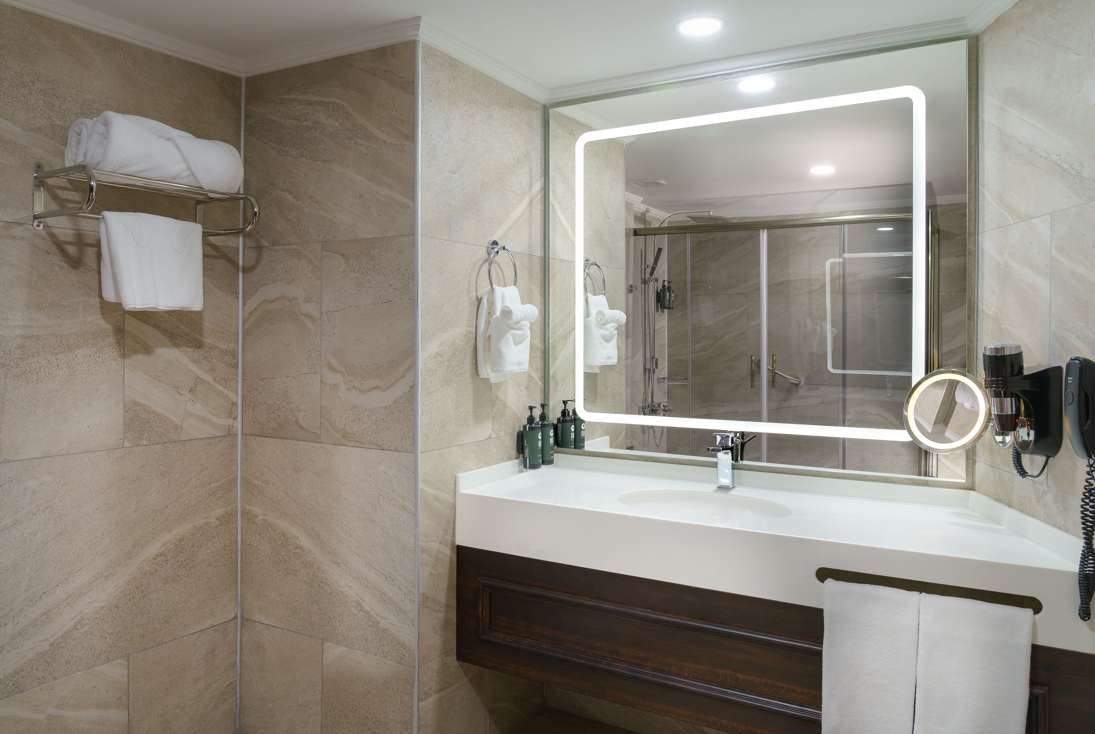 A modern bathroom with a large mirror, a glass shower enclosure, and a vanity with a dark wood cabinet.