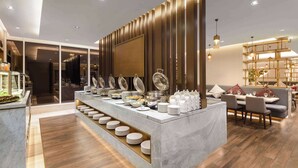 A modern hotel dining area with a buffet setup, marble countertops, and a seating area with tables and chairs. - Ramada By Wyndham Riyadh King Fahd Road (Riyadh)