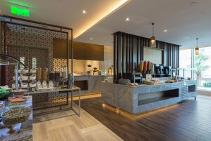 A modern hotel lobby with a marble reception desk, a coffee station, and a decorative partition with geometric patterns.