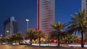 A tall building with "RAMADA" signage, surrounded by palm trees and streetlights. - Ramada By Wyndham Riyadh King Fahd Road (Riyadh)