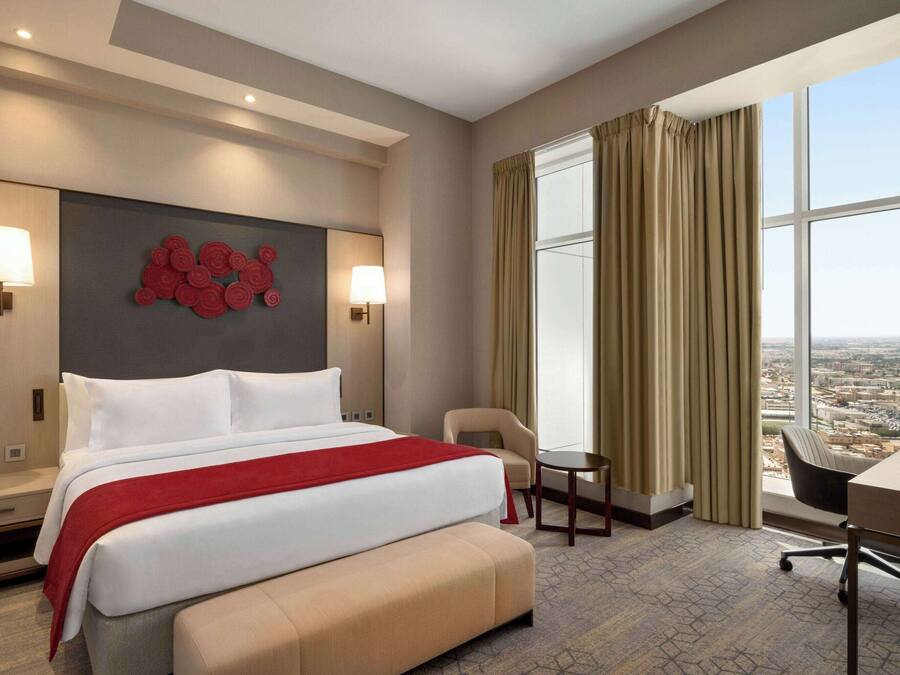 A hotel room with a large bed, a desk, a chair, and a view of the city.
