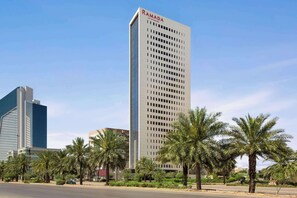 A tall building with the name "RAMADA" on top, surrounded by palm trees and other greenery. - Ramada By Wyndham Riyadh King Fahd Road (Riyadh)